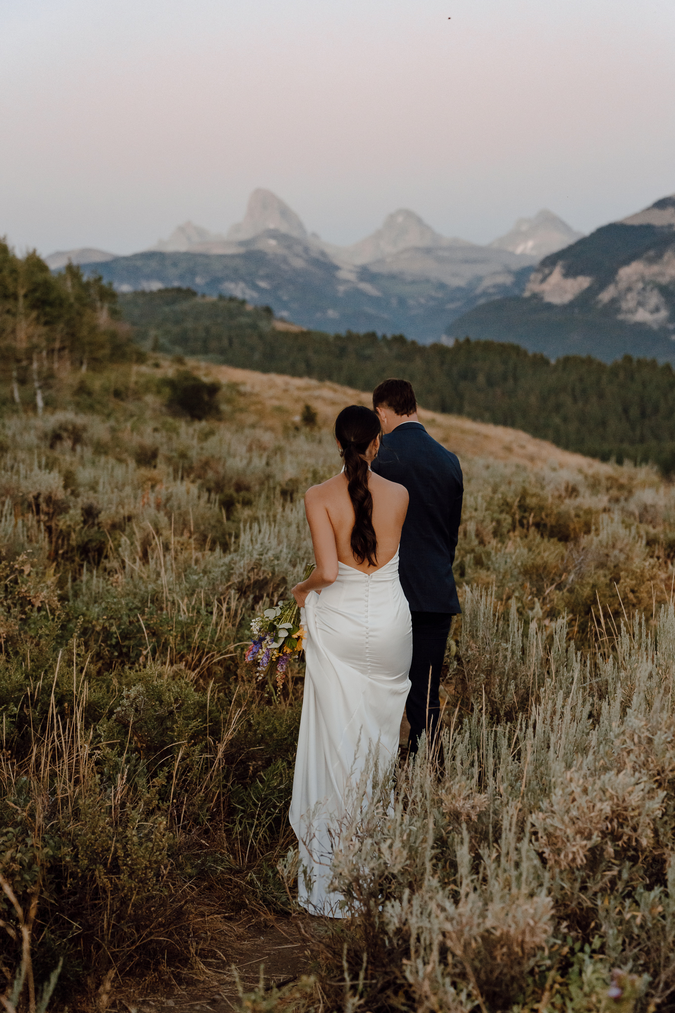 Couple walks beneath the Teton mountains while doing bridals